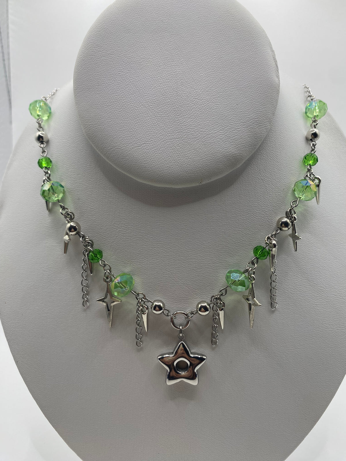 A gothic-style beaded necklace with green faceted beads, silver lightning bolts, and a central silver star charm, displayed on a white mannequin bust.