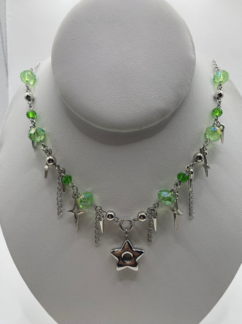 A gothic-style beaded necklace with green faceted beads, silver lightning bolts, and a central silver star charm, displayed on a white mannequin bust.